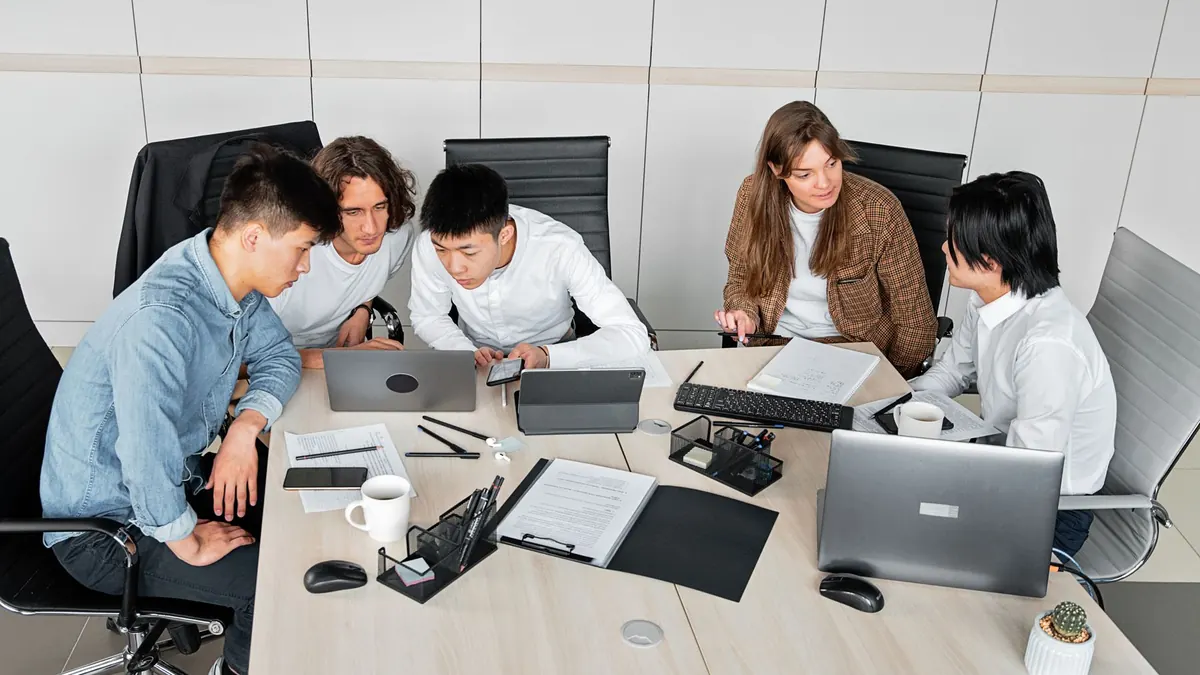 Colleagues around a meeting table reviewing documents and laptops together