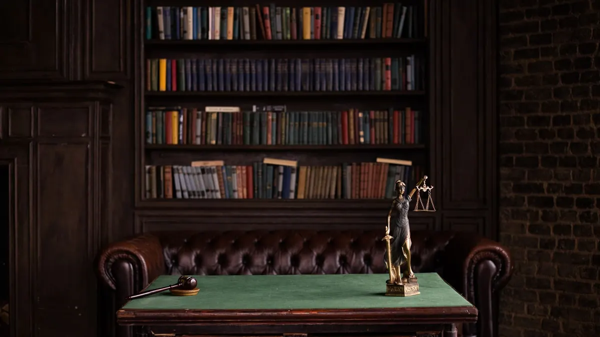 A bronze Lady Justice figurine and a gavel on a desk in front of law books